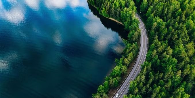 Aerial view of a road winding through a forest and a lake